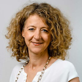 Lächelnde Frau mit lockigen braunen Haaren und weißer Bluse